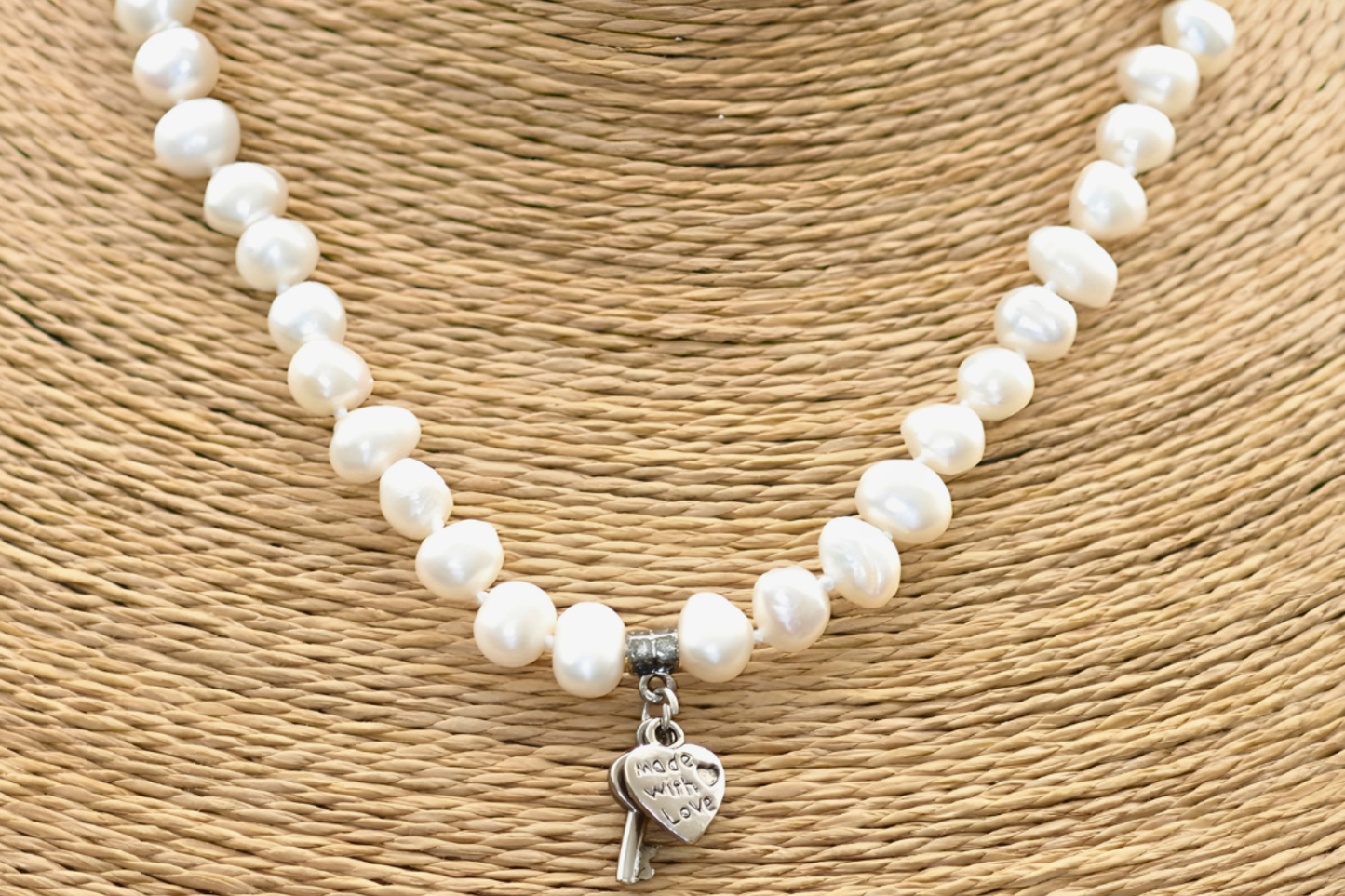 Pearl necklace with a silver heart charm on a textured beige background