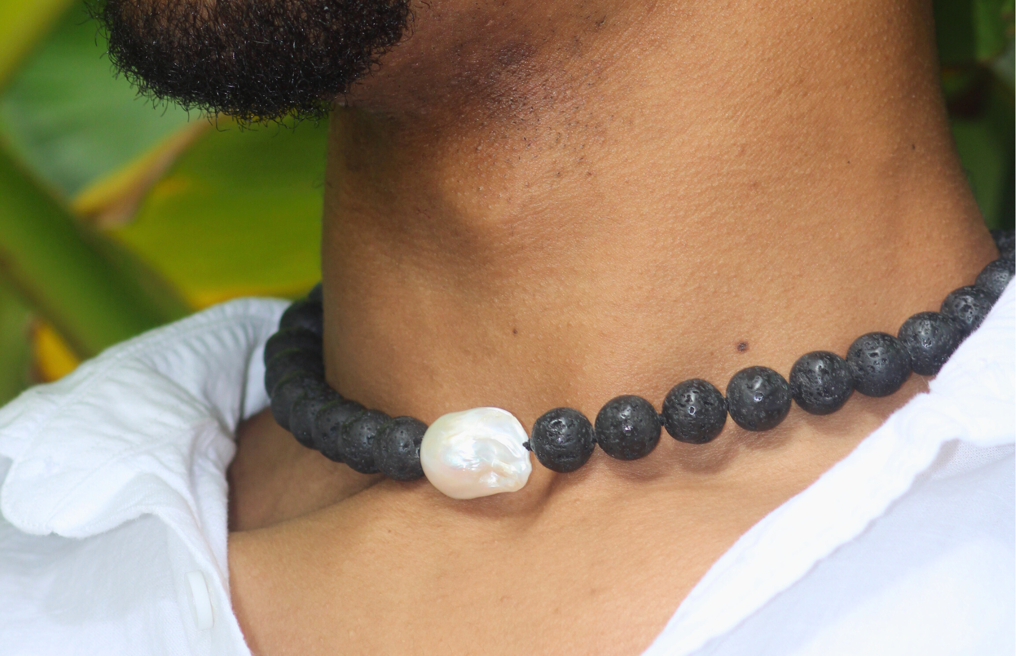 Person wearing a black beaded necklace with a central pearl against a blurred green background