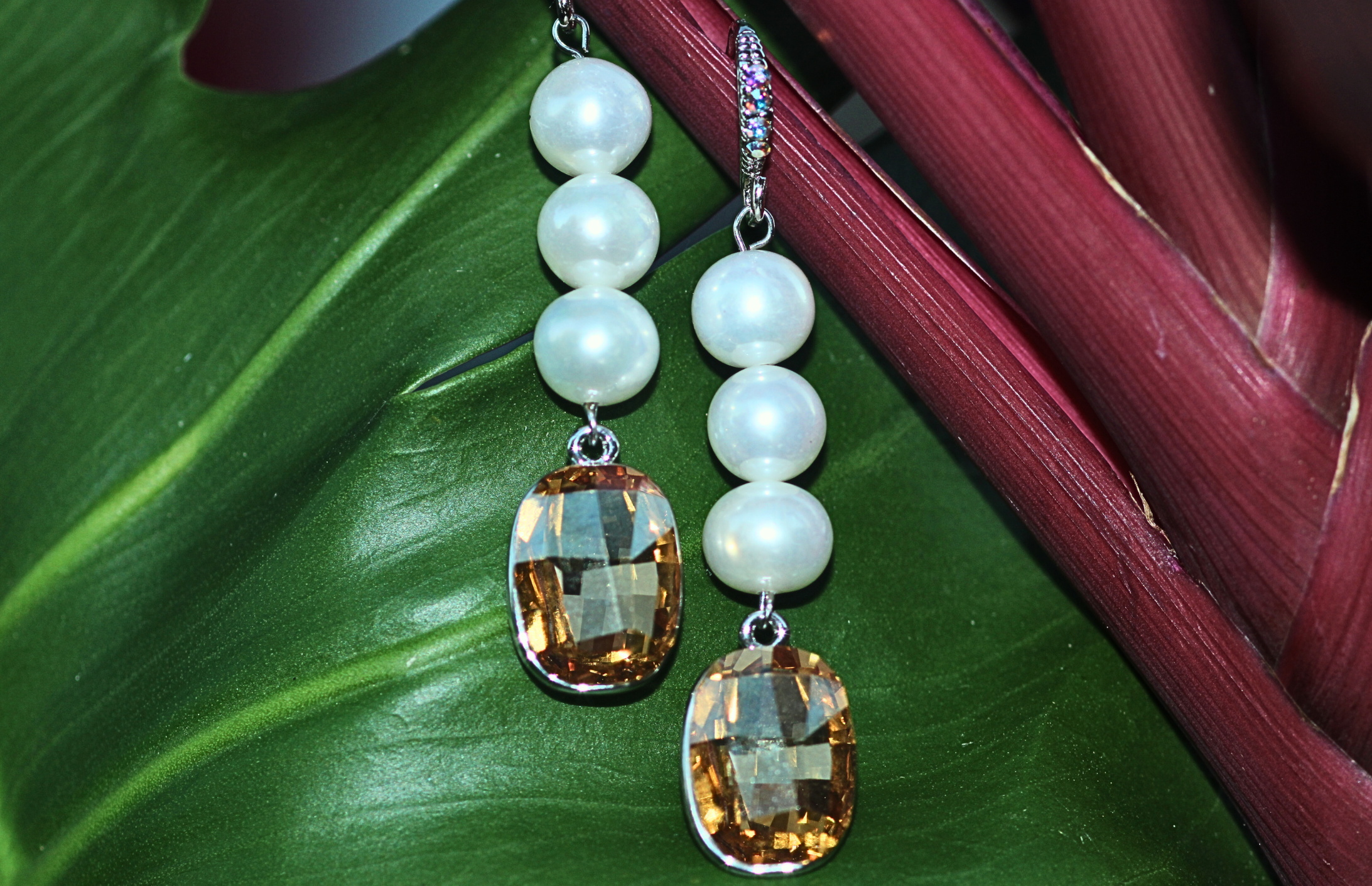 Pair of earrings with white beads and brown teardrop-shaped stones on a green leaf background